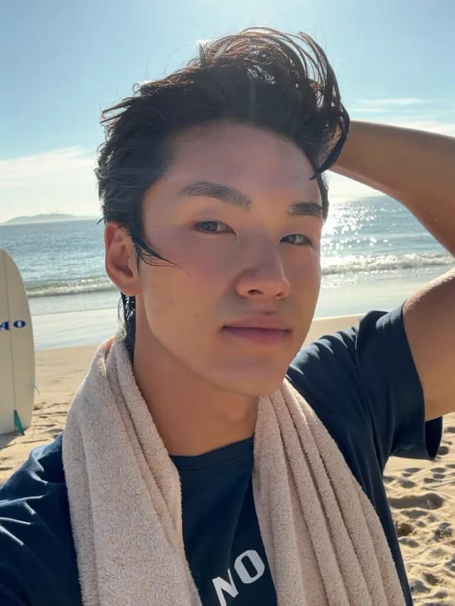 Jeune homme serviette autour du cou repoussant ses cheveux mouillés sur une plage ensoleillée après le surf – Higgsfield Soul 2