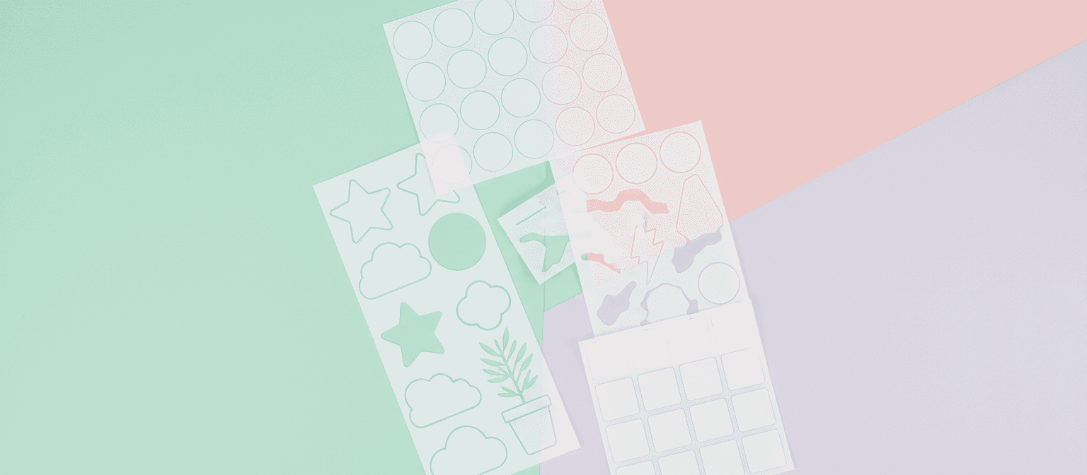 다양한 모양의 빈 비닐 스티커들이 파스텔 톤의 책상 위에 예술적으로 배열되어 있으며, 맞춤 디자인에 적합합니다.