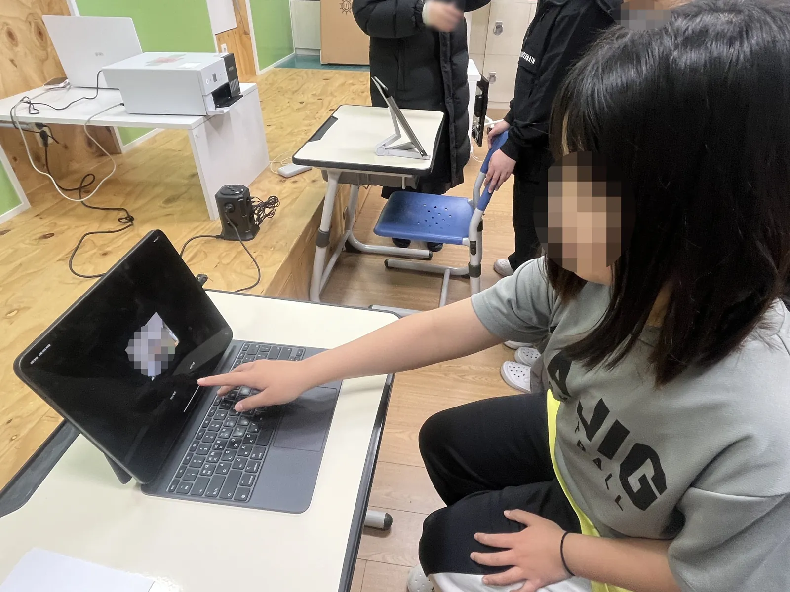 노트북으로 자기 사진을 올리는 학생과 뒤편 책상에 놓인 포토프린터